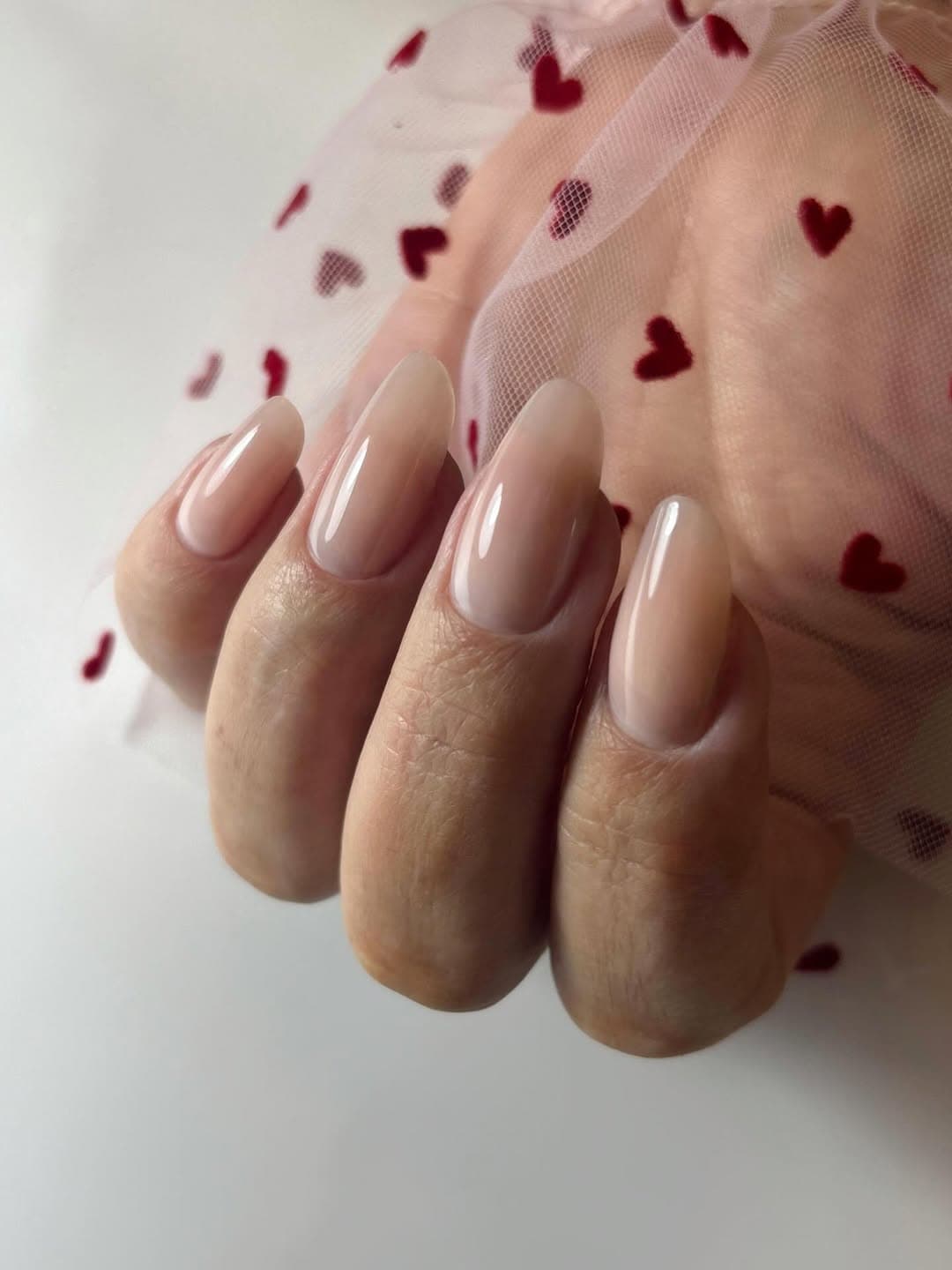 Lange nude amandelnagels op een zachte hartstof achtergrond